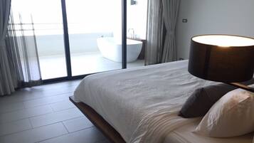 Un dormitorio moderno con una cama grande, una lámpara de noche y vista a un baño a través de una puerta de cristal.