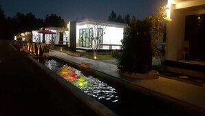 Un edificio moderno con fuente en primer plano, rodeado de zonas bien iluminadas y vegetación escasa.