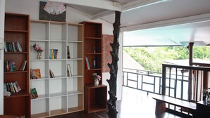 A spacious room with a large bookshelf filled with books and decorative items, a wooden bench, and a view of greenery outside. - Lantern Inn Koh Lipe (Koh Lipe)