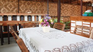 A dining area with wooden tables and chairs, a white tablecloth, and a woven wall. - Lantern Inn Koh Lipe (Koh Lipe)