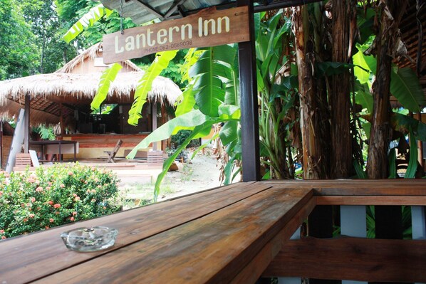 Un banco de madera con un cenicero de vidrio, una estructura con techo de paja y un letrero que dice "Lantern Inn".