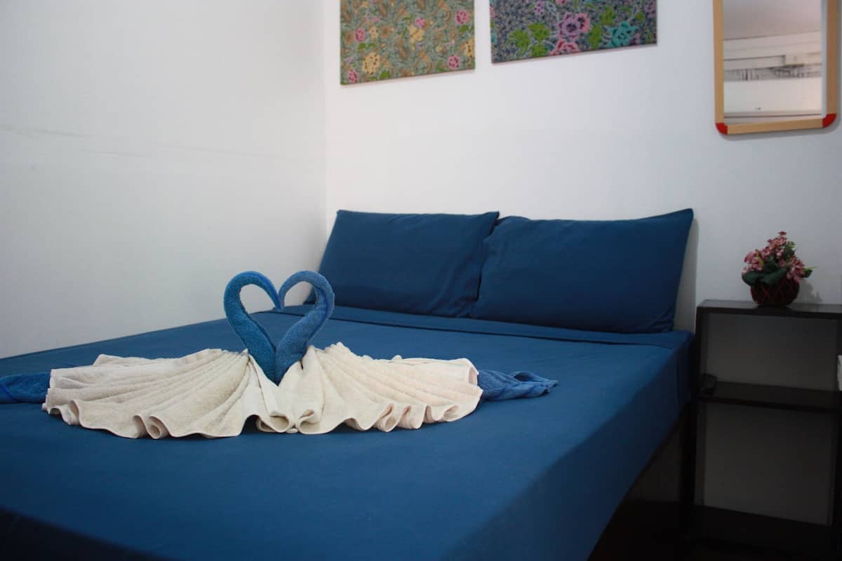 Un lit bien fait, avec une literie bleue et une serviette pliée en forme de cœur.