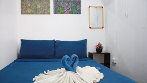 A neatly made bed with blue bedding, a heart-shaped towel arrangement, and two floral wall art pieces. - Lantern Inn Koh Lipe (Koh Lipe)