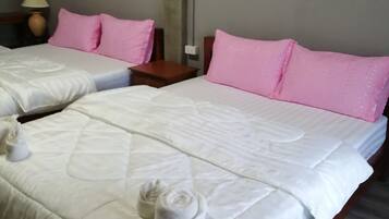 Habitación de hotel con dos camas, cada una con ropa blanca y almohadas rosas. Hay una mesita con una lámpara y un adorno en la pared.