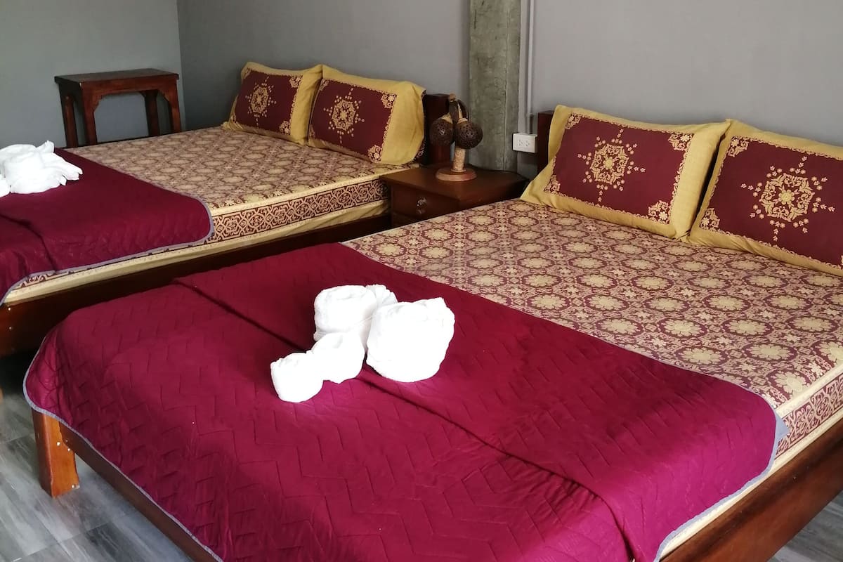 Two single beds with red and patterned bedding, a wooden nightstand, and a small table.