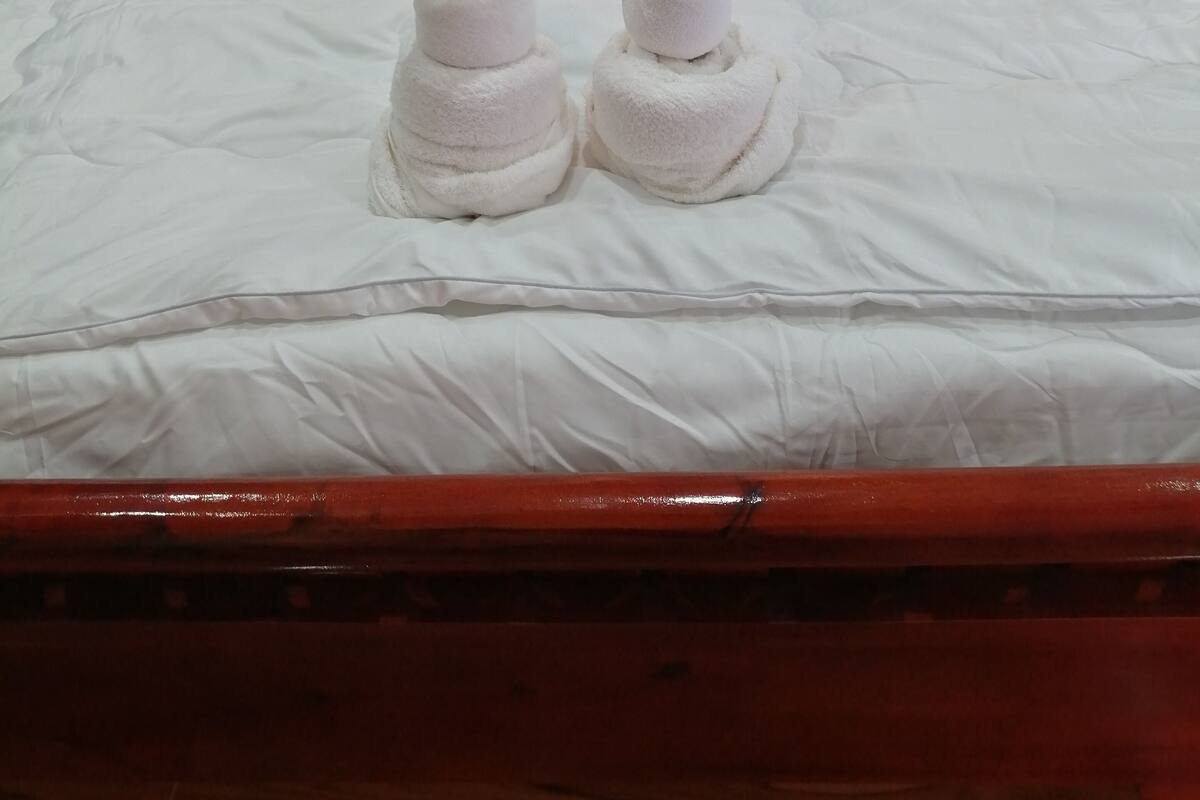 A neatly made bed with white linens and two towels shaped like animals.