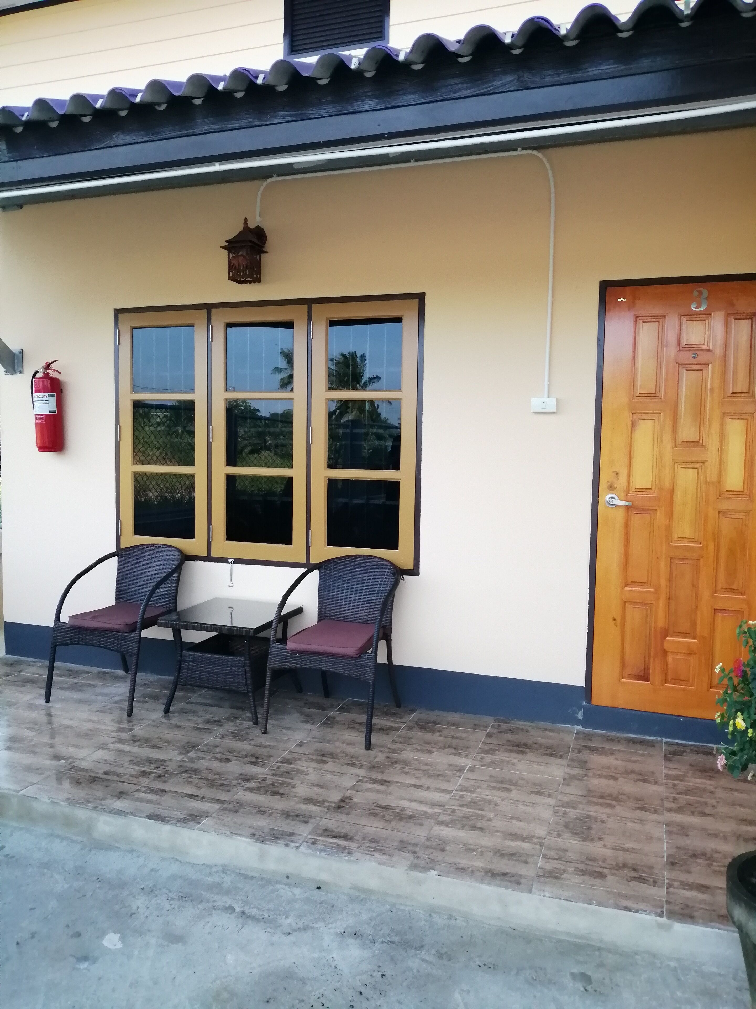 Un edificio con entrada de baldosas, puerta de madera y un extintor colgado en la pared.