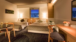 Een hotelkamer met twee bedden, een kleine tafel met stoelen, een bureau en een raam met uitzicht op de stad.