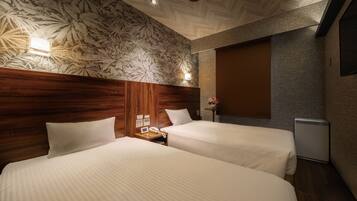 Habitación de hotel con dos camas, cabecero de madera, papel tapiz floral, lámparas de noche, una mesita con un teléfono y un televisor fijado a la pared.
