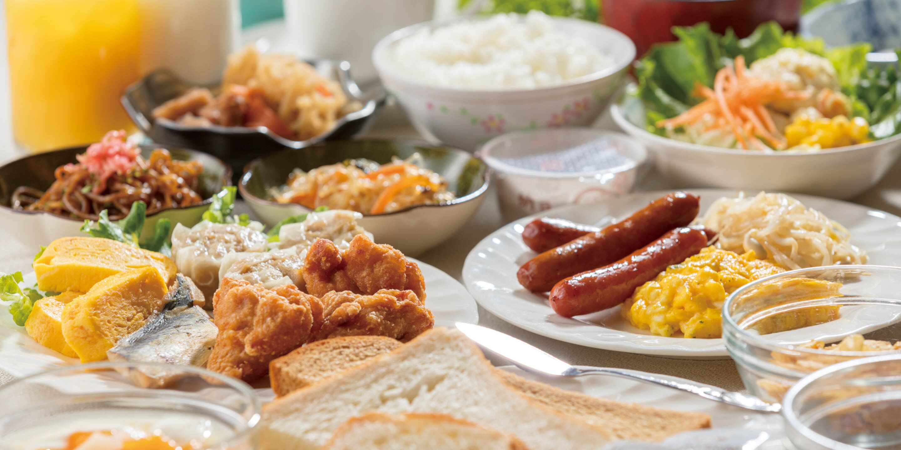 Una mesa con diferentes platos, incluyendo salchichas, pollo frito, arroz y verduras.