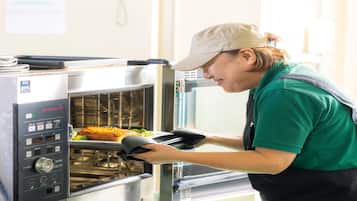 A person in a green shirt and apron using an oven mitt to handle food in a commercial oven.