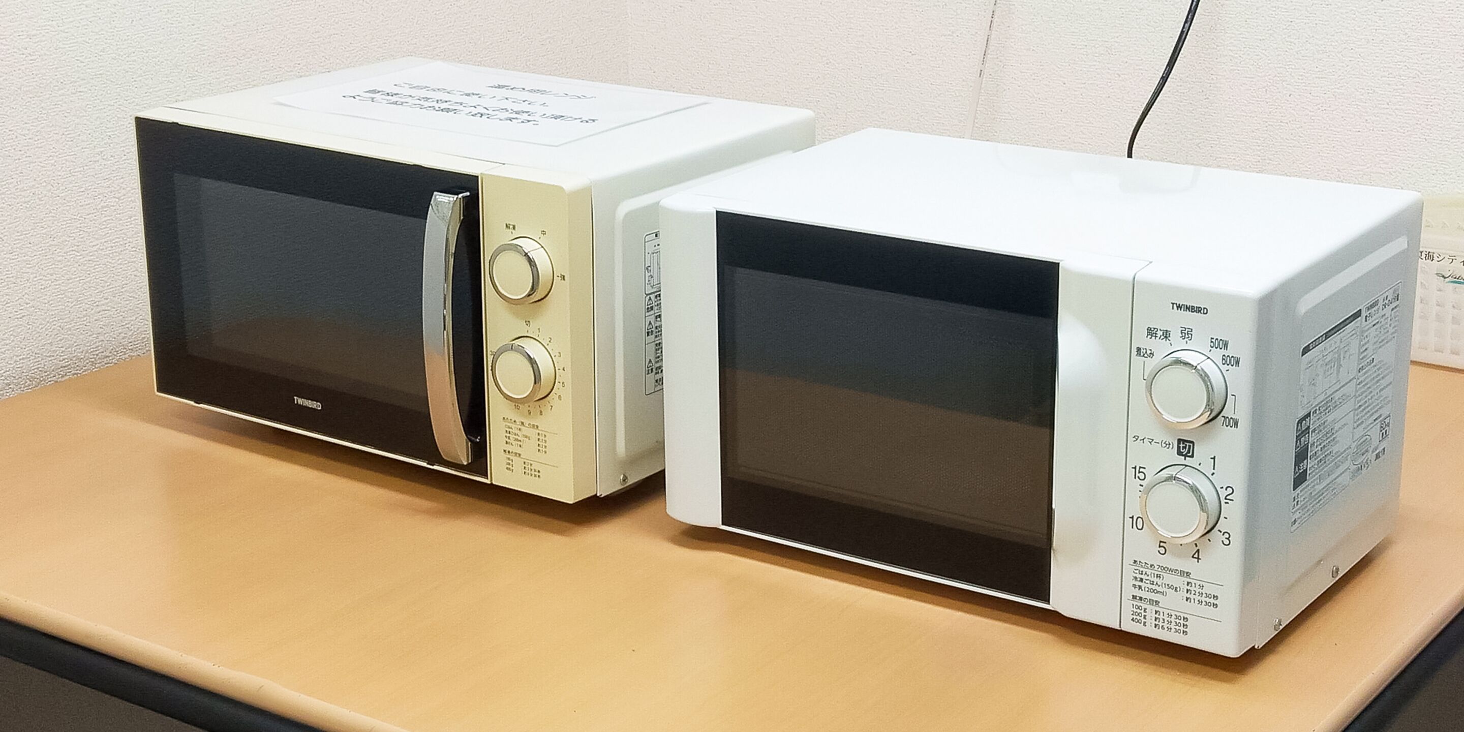 Two microwave ovens on a wooden table.