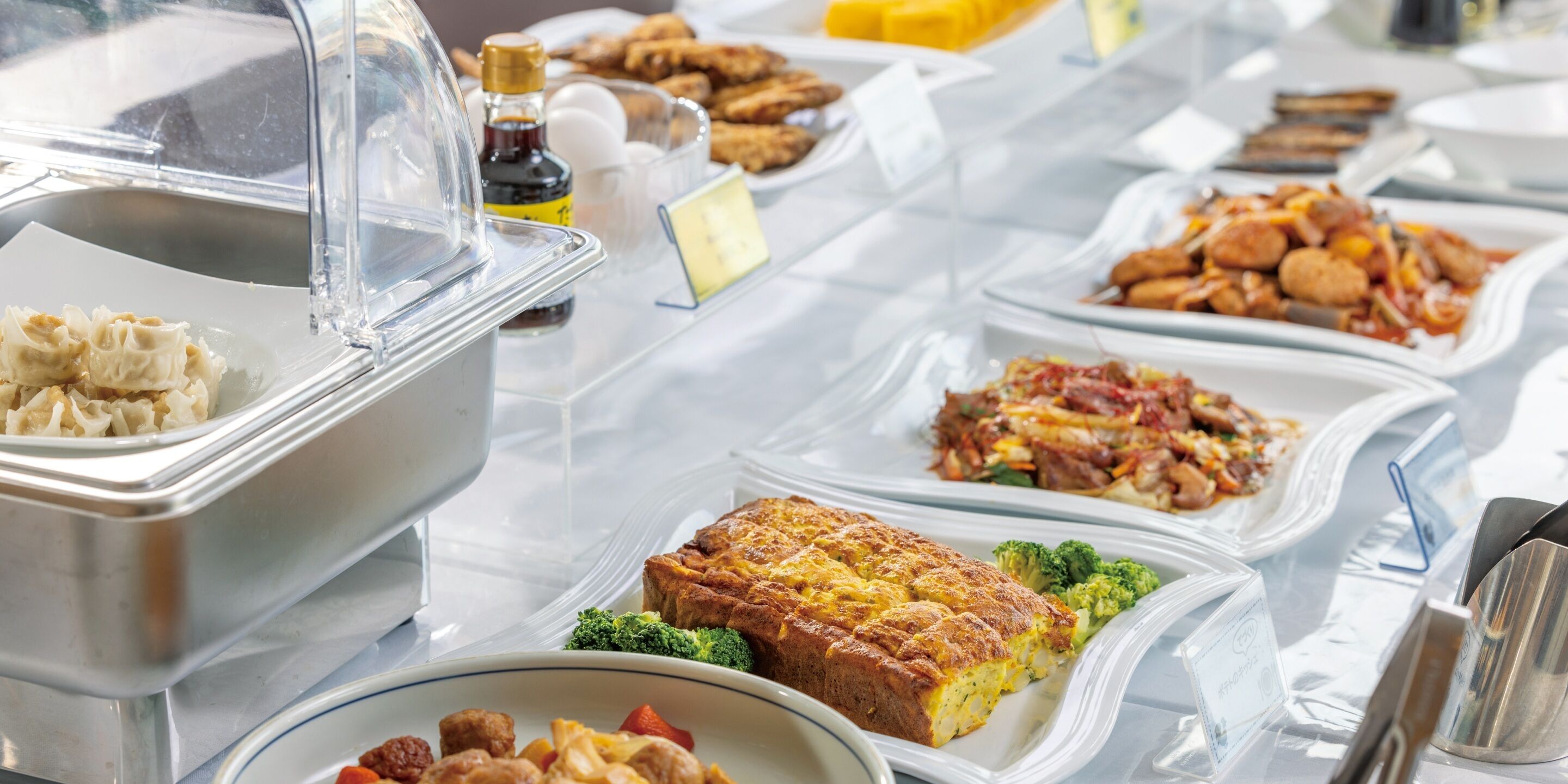Un buffet proposant divers plats, notamment une quiche, des brocolis et un assortiment d’autres aliments préparés.