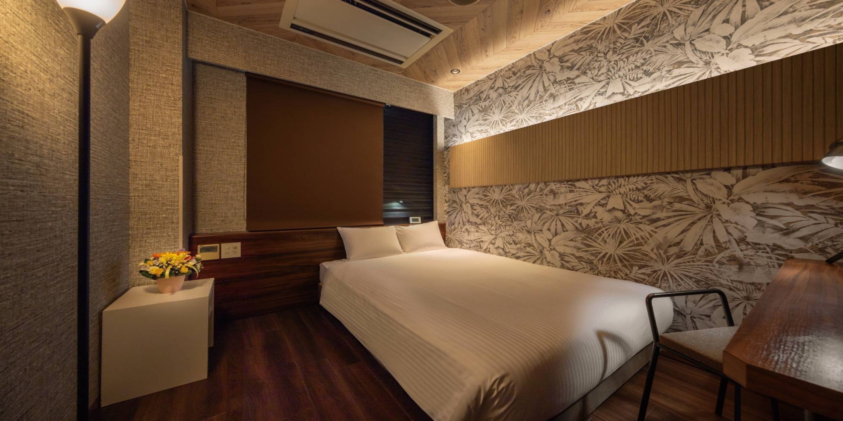 Un dormitorio con una cama grande, cabecera de madera, mesita de noche con un florero y pared con estampado floral.