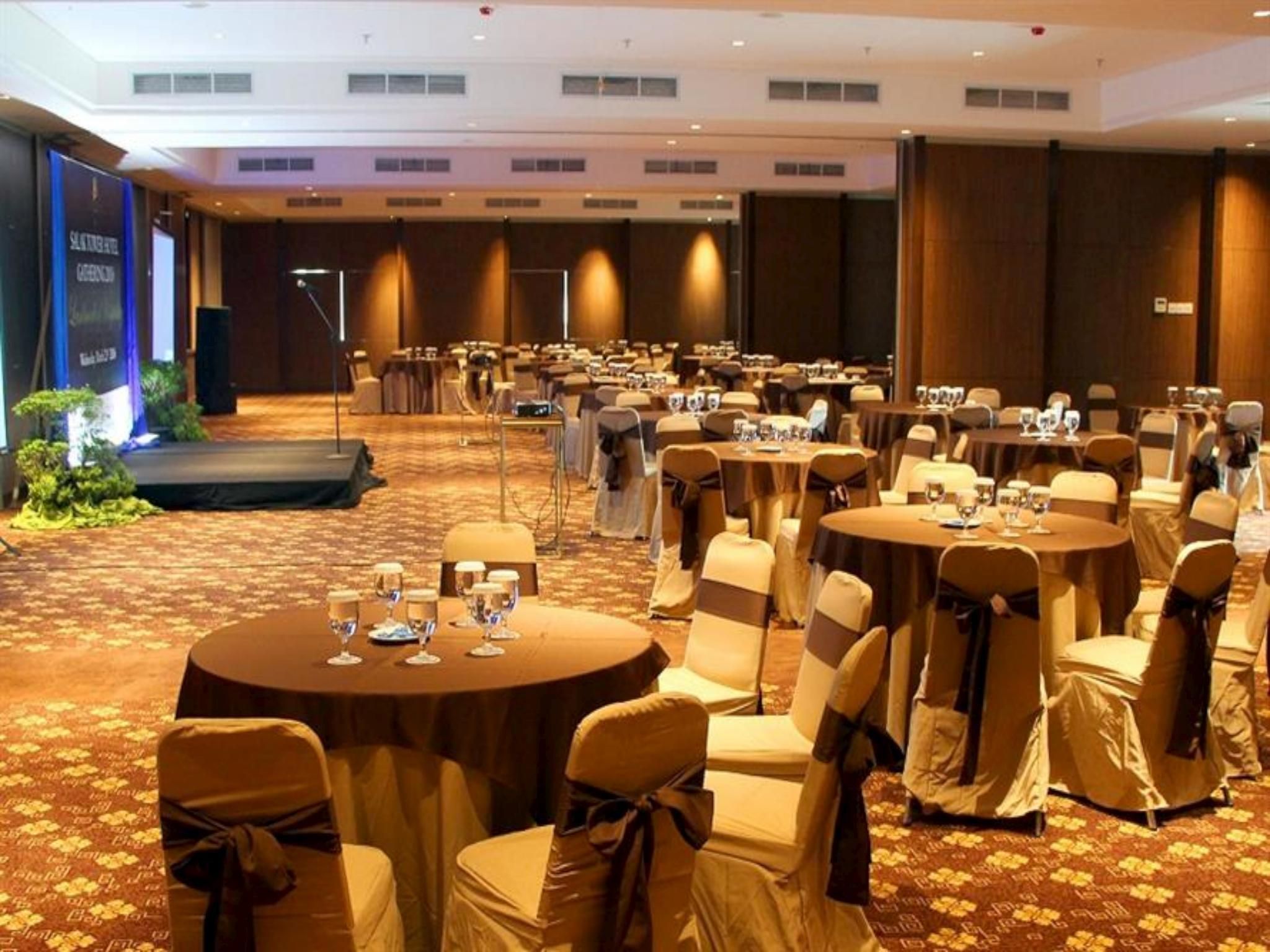 Un salón de conferencias con mesas redondas, sillas y un escenario.