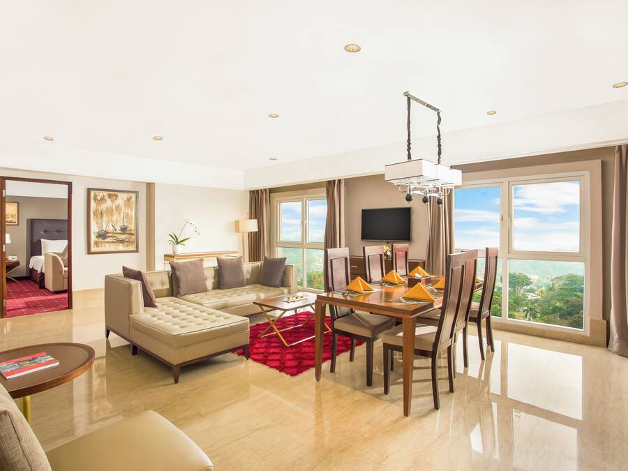 A hotel room with a living area, dining table, and large windows.