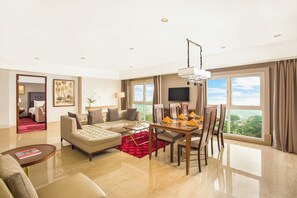 A hotel room with a living area, dining table, and large windows. - Swiss-belhotel Bogor (Bogor)