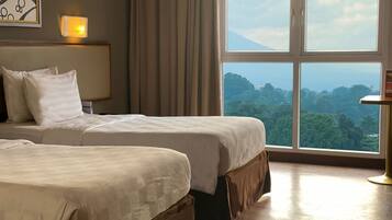 A hotel room with two beds, a large window with a view, and a bedside table with a lamp.