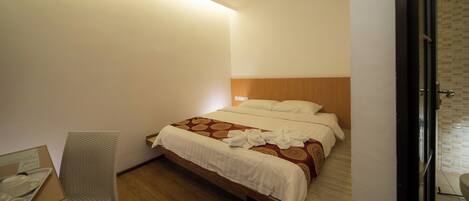 Una habitación de hotel con cabecera de madera, una cama con colcha estampada y una mesita de noche con lámpara.