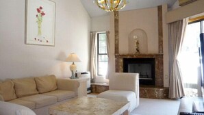 Un salon comprenant un canapé, un fauteuil et une table basse. On y trouve une cheminée avec un manteau de cheminée et un lustre.