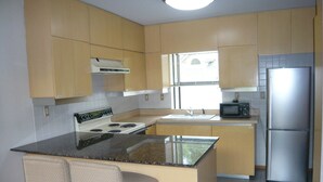 Une cuisine avec des meubles en bois, un réfrigérateur en acier inoxydable, un four à micro-ondes, une cuisinière et deux tabourets de bar.