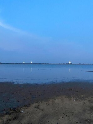A calm body of water with a sandy shore and three white boats in the distance.