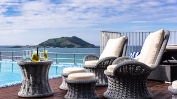 Zona junto a la piscina con mobiliario de mimbre y vista al mar.