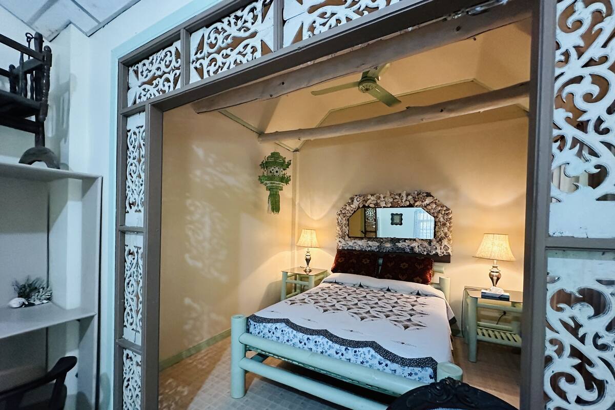 A bedroom with a bed, two bedside tables with lamps, a ceiling fan, and decorative wall panels.
