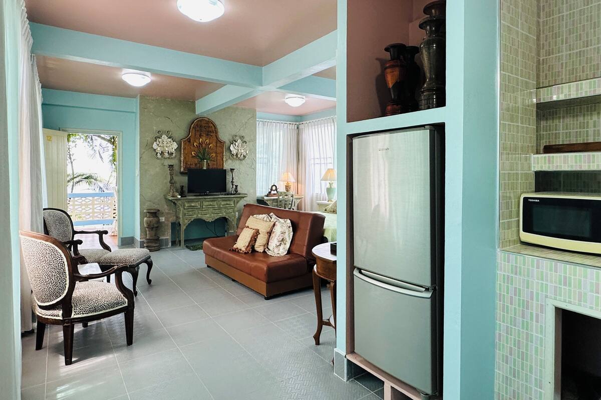 A living room with a sofa, chairs, a television, and a refrigerator.