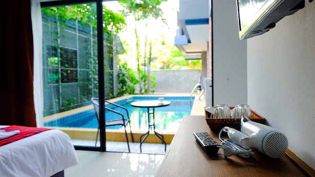 Quarto de hotel com cama, mesa com secador de cabelo e controle remoto, TV e vista para uma piscina ao ar livre.