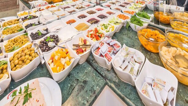 Een buffet met diverse soorten eten in kommen en op schalen, zoals olijven, fruit en dips.