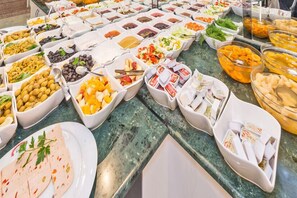 Un bufé con diversos alimentos en cuencos y platos, como aceitunas, frutas y salsas.