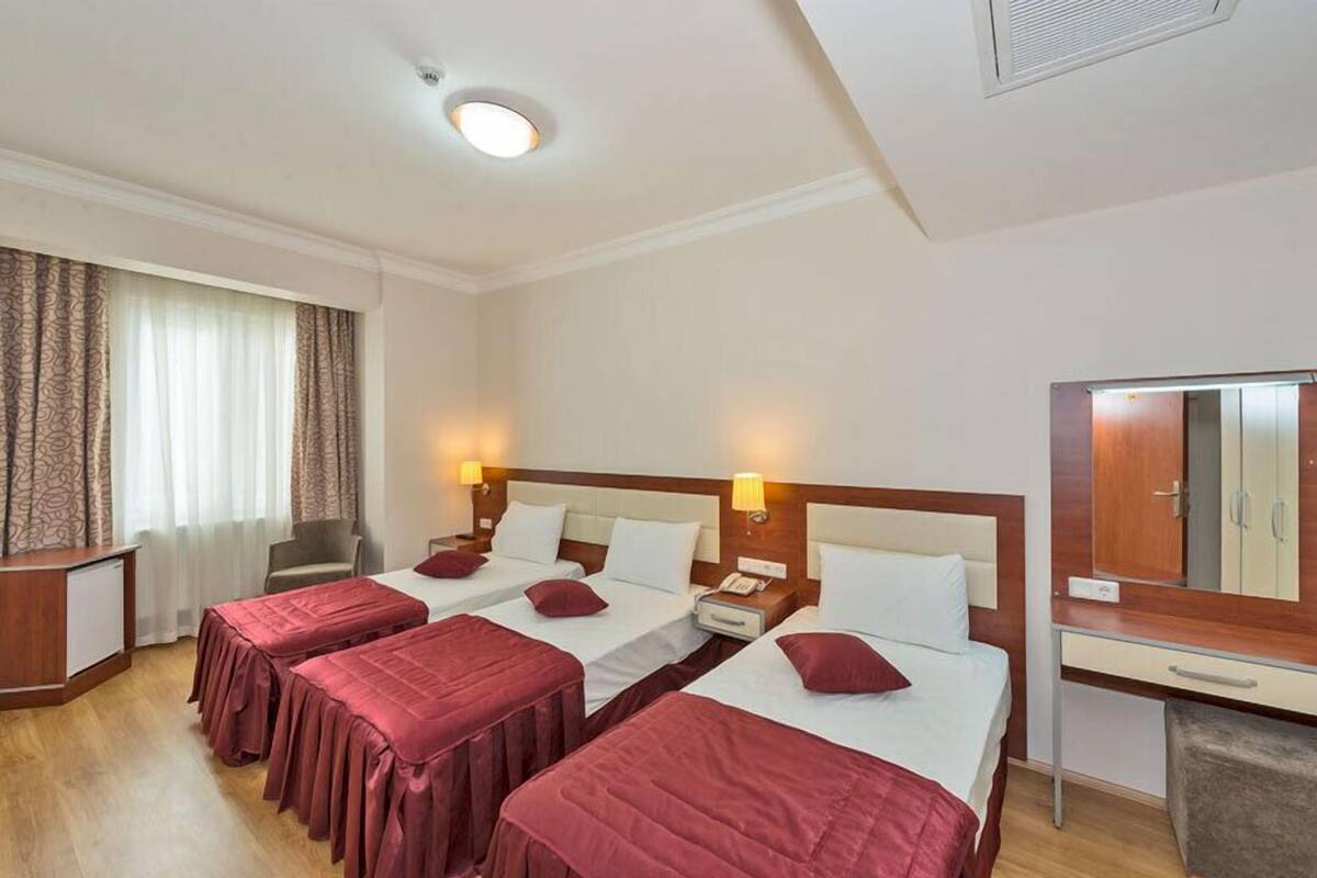 A hotel room with two beds, a desk, a chair, a mirror, and a window with curtains.