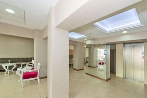 A spacious lobby with a high ceiling, skylights, a seating area with white chairs and a red cushion, and a glass partition reflecting the interior. - La Garden Hotel (Istanbul)