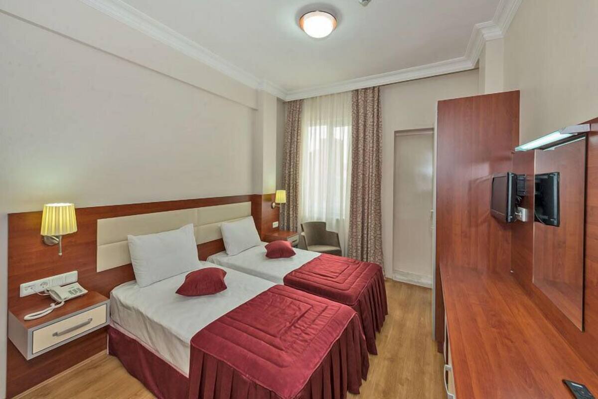 A hotel room with two beds, a TV, a desk with a lamp, and a phone.