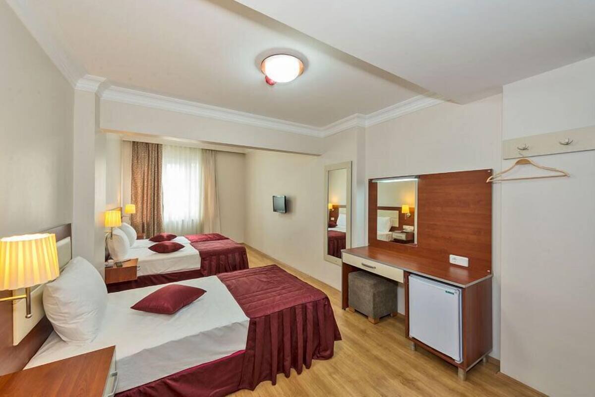 A hotel room with two beds, a desk, a mirror, a TV, and a small refrigerator.