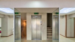 Een moderne liftruimte met twee liften, elk aan één kant, en een centrale trap.