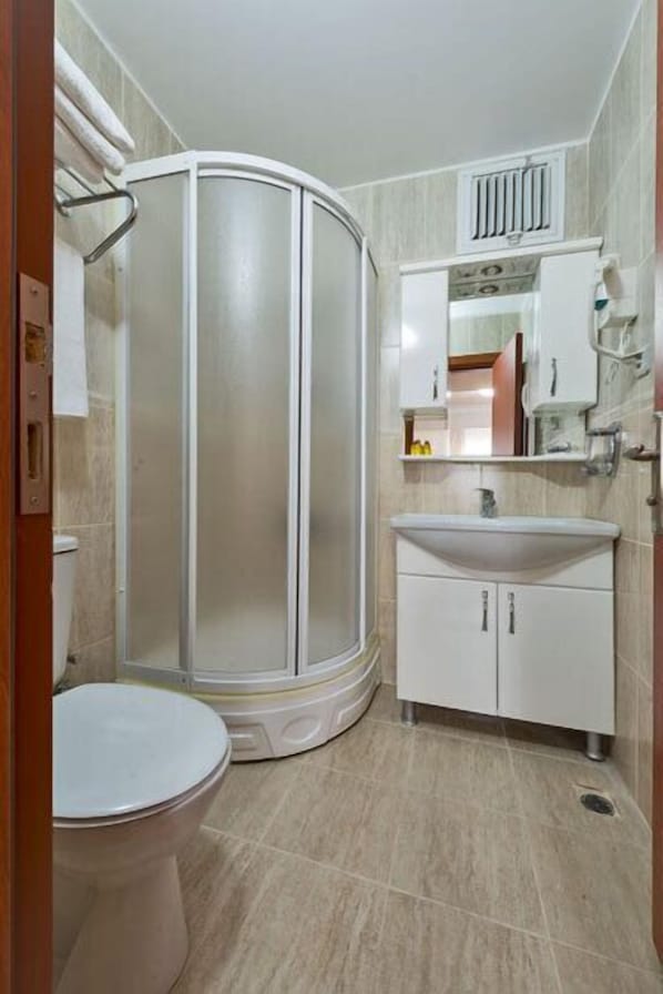 A bathroom with a toilet, a shower enclosure, a sink, and a cabinet.