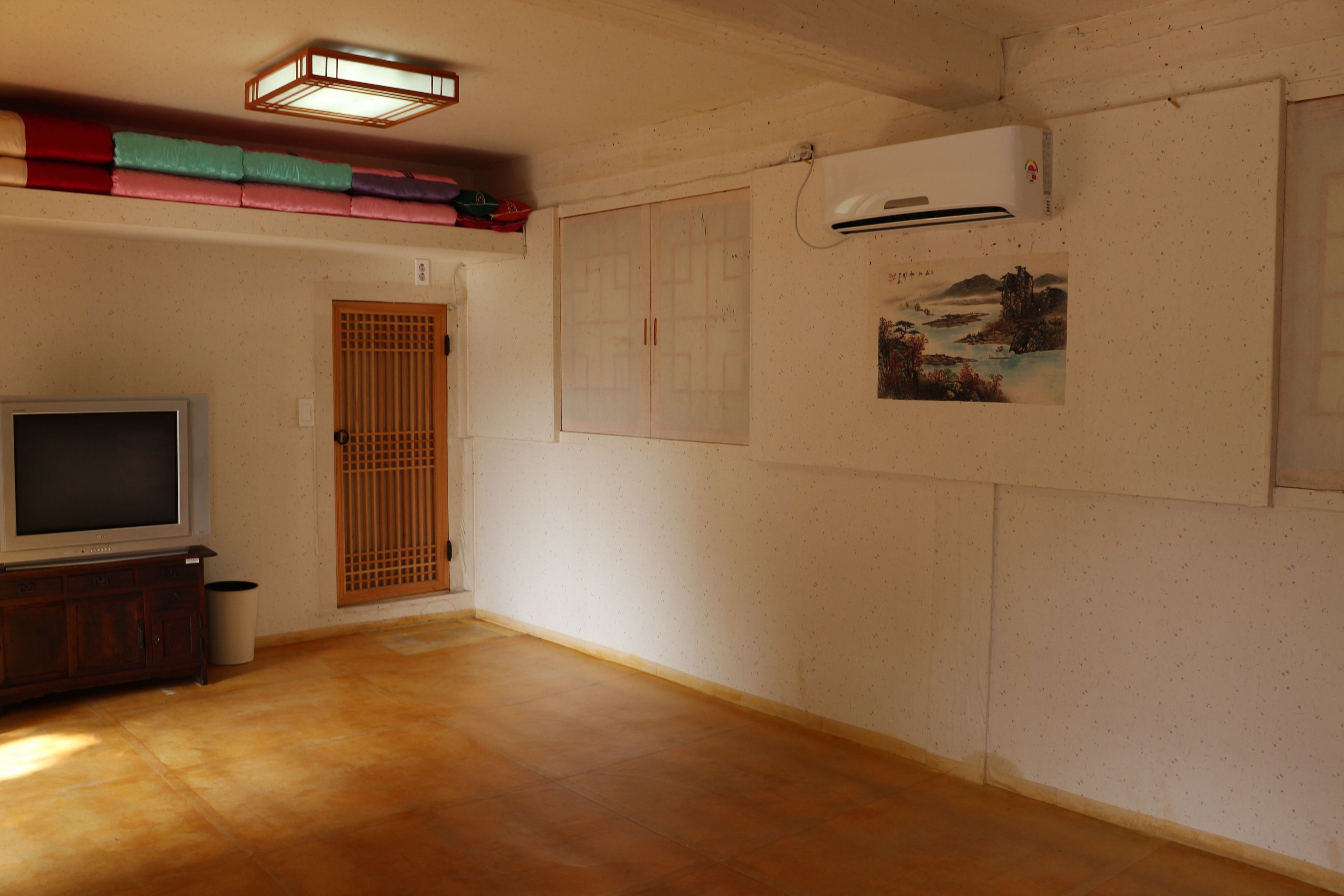 A room with a wooden floor, a television, a wardrobe, and an air conditioning unit.