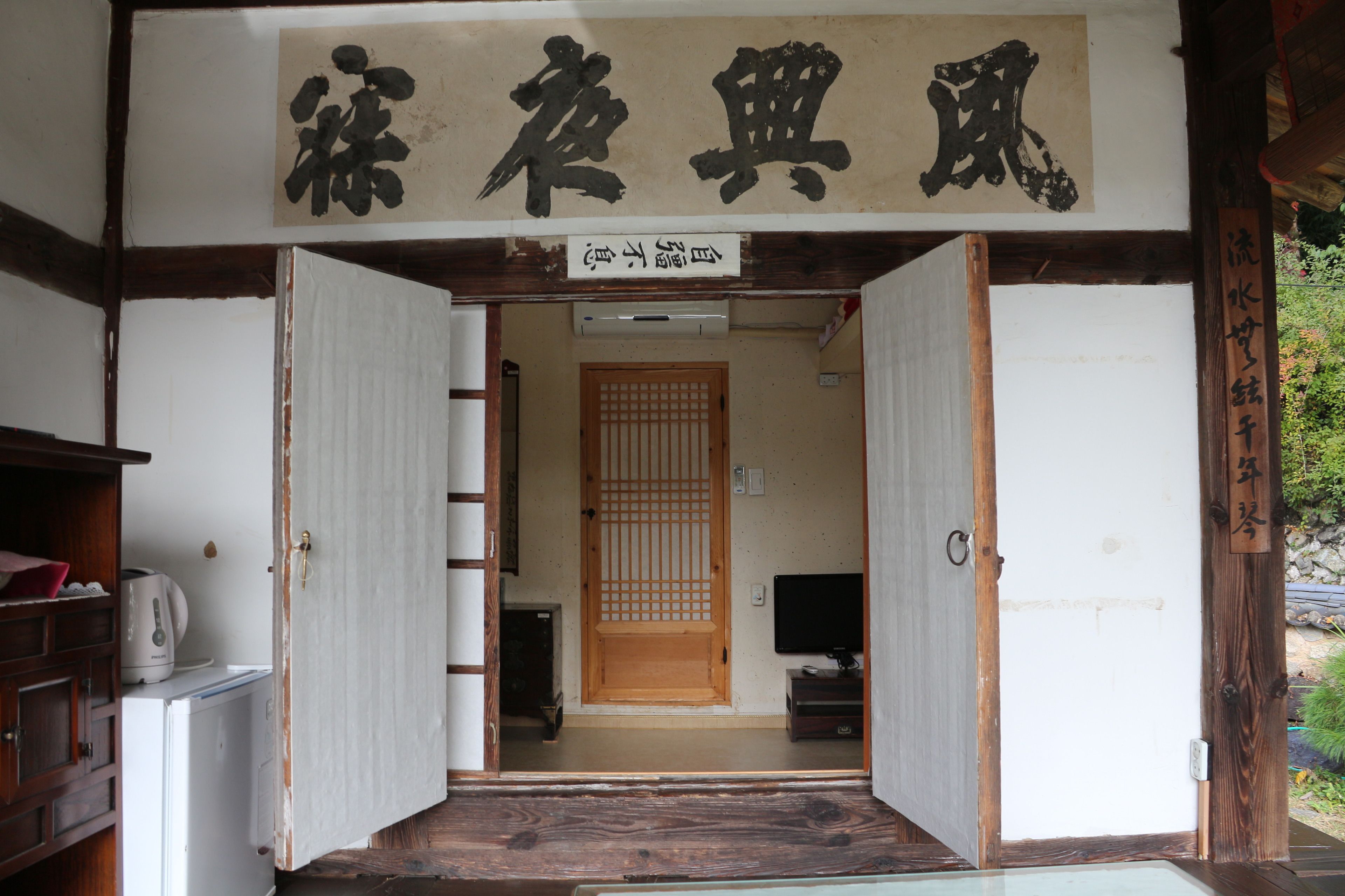 A traditional Japanese room with tatami flooring, a wooden door, and a television.