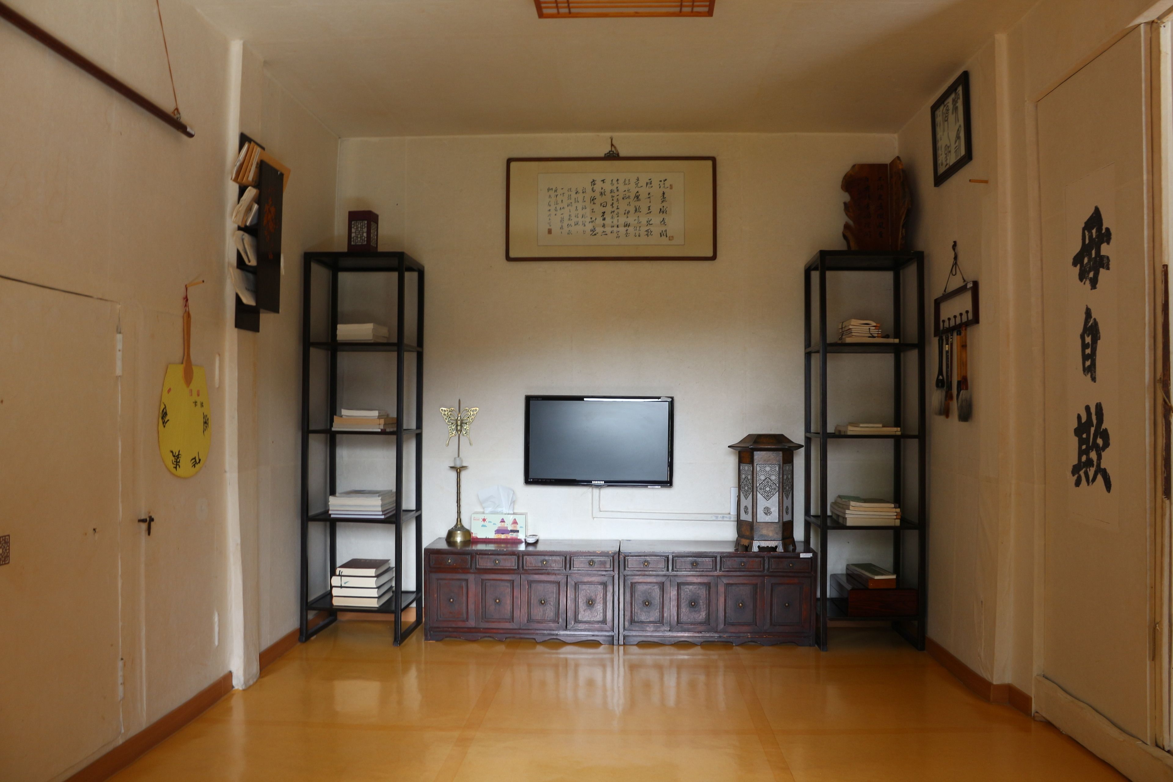 A living room with a wooden floor, a flat-screen TV mounted on the wall, and two bookshelves on either side.