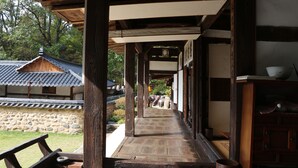 A traditional wooden corridor with stone flooring, leading to a building with a tiled roof. - Chiam Gotaek (Andong)