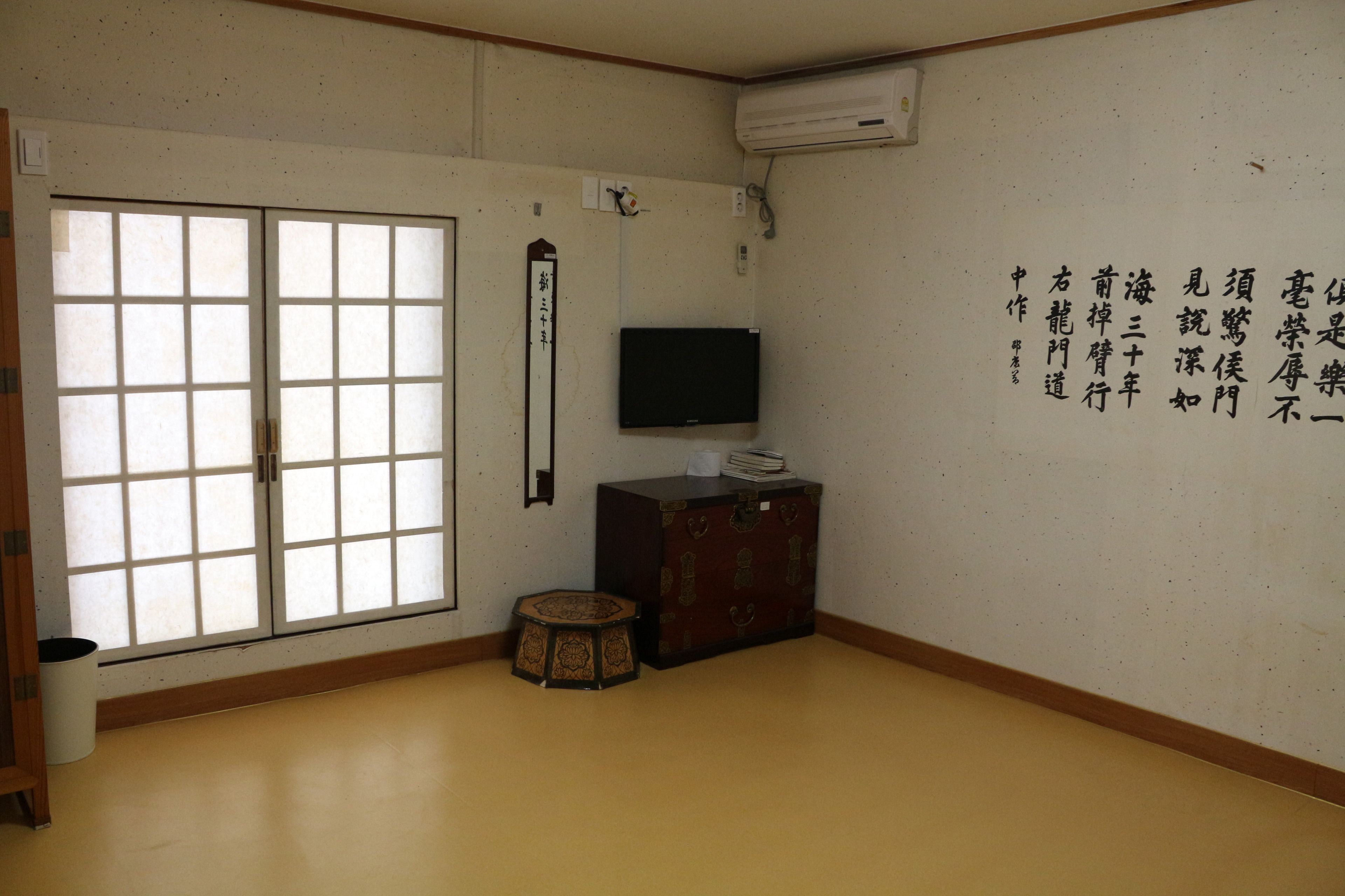 Een traditionele Japanse kamer met tatami vloerbedekking, een schuifdeur, een televisie op een kast en kalligrafie aan de muur.