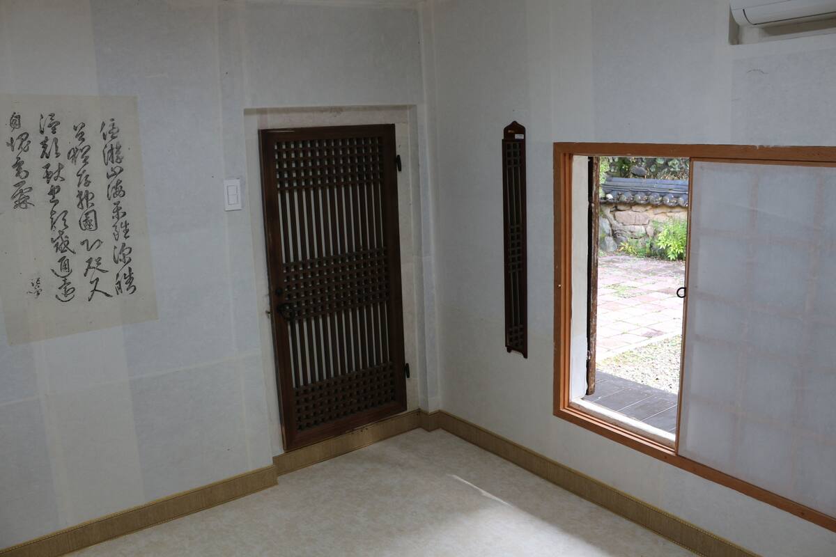 A room with a traditional sliding door, a small window, and a wall-mounted paper with Japanese characters.
