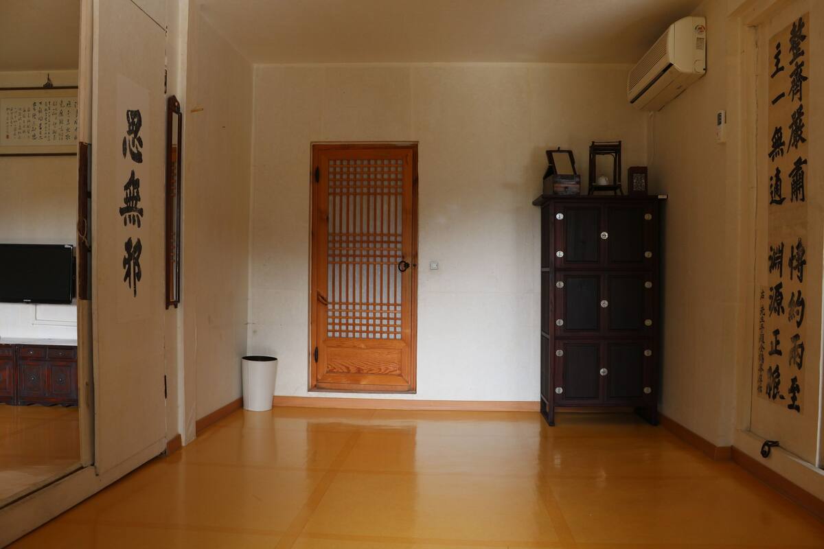 A traditional Japanese room with a wooden sliding door, a dark wooden cabinet, and a white trash bin.