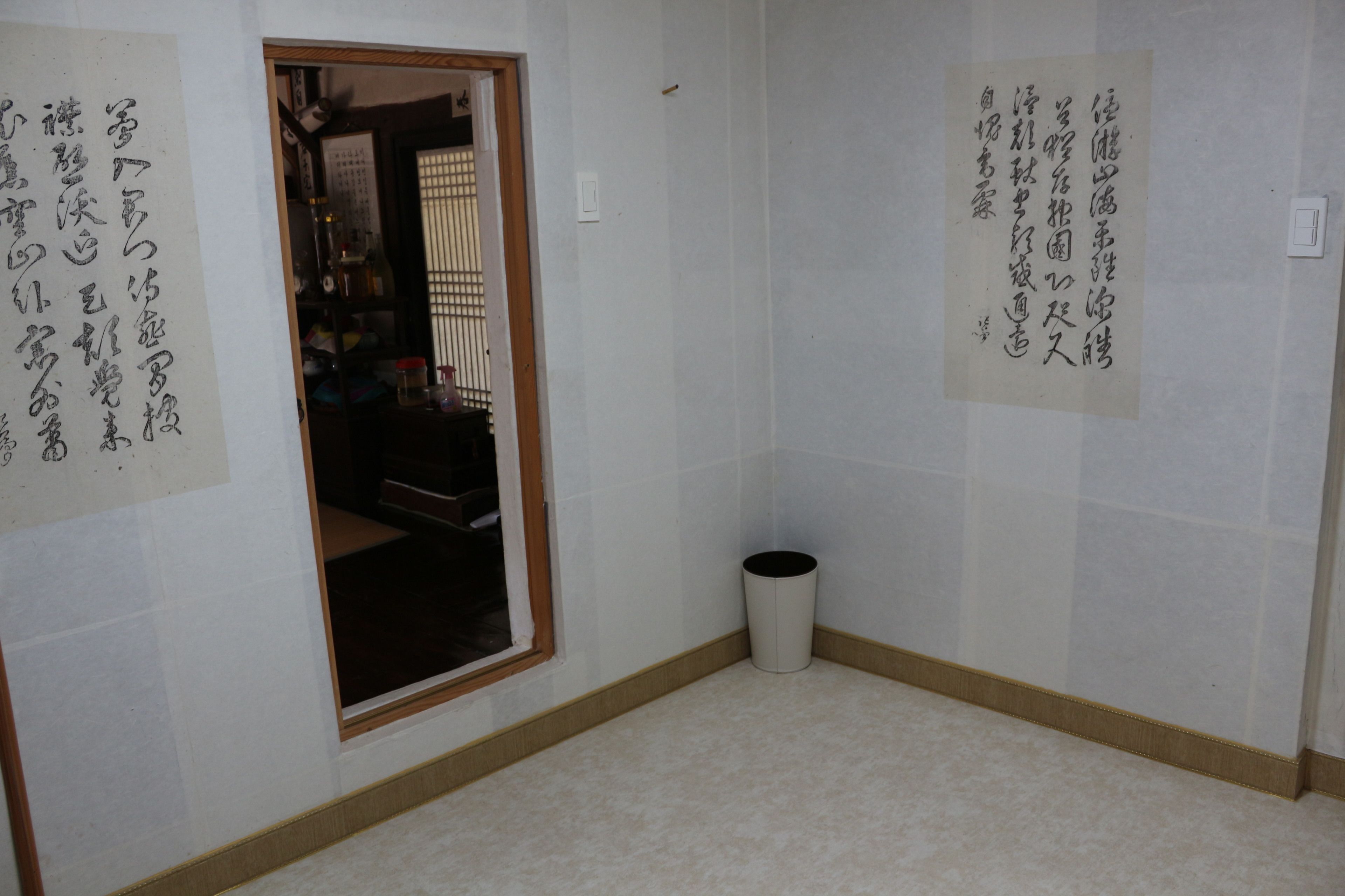 Una habitación con una puerta de madera, un cubo de basura pequeño y dos hojas de papel con texto en japonés en las paredes.