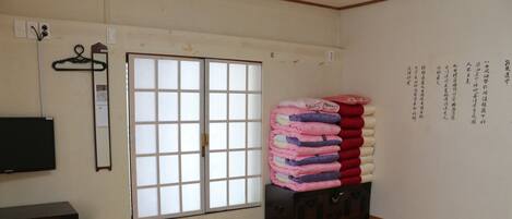 A room with a sliding door, a stack of folded blankets, a wooden chest, and a wall-mounted television.