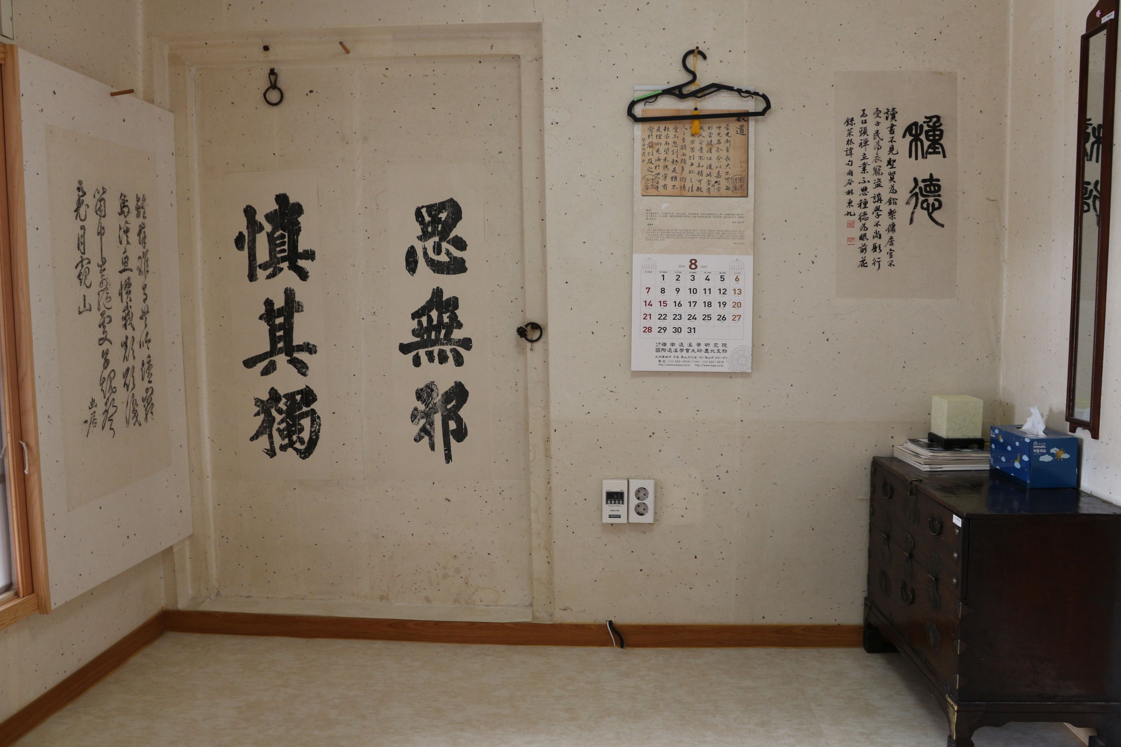 Una habitación con estética japonesa tradicional, que incluye caligrafía en las paredes, un armario de madera y un calendario.