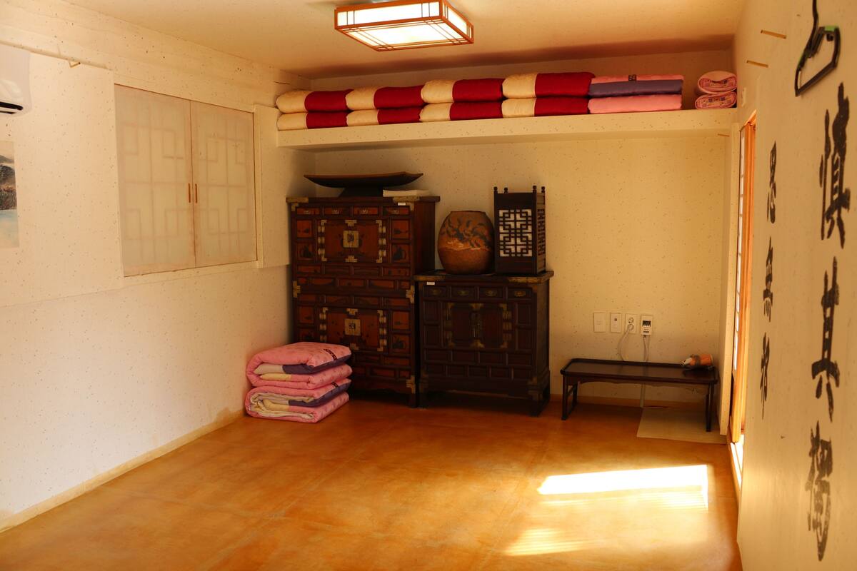 A room with a wooden floor, a bed with a red and white striped blanket, a wooden cabinet, and a wall with calligraphy.