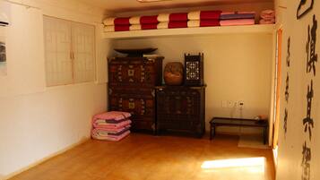 Ein Zimmer mit Holzboden, einem Bett mit rot-weiß gestreifter Decke, einem Holzkasten und einer Wand mit Kalligraphie.